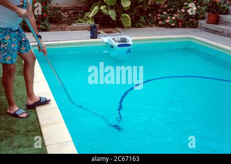 Persona che pulisce e clorurando la piscina in un caldo pomeriggio estivo, sta facendo funzionare il pulitore e aggiungendo polvere di cloro Foto Stock