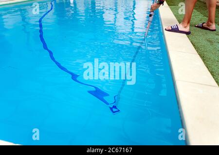 Persona che pulisce e clorurando la piscina in un caldo pomeriggio estivo, sta facendo funzionare il pulitore e aggiungendo polvere di cloro Foto Stock