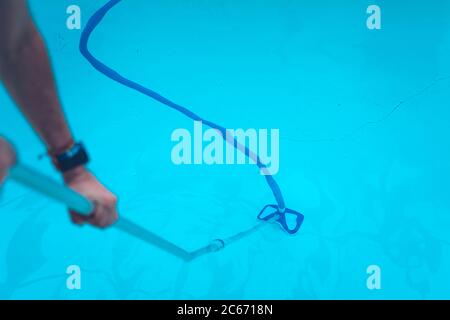 Persona che pulisce e clorurando la piscina in un caldo pomeriggio estivo, sta facendo funzionare il pulitore e aggiungendo polvere di cloro Foto Stock