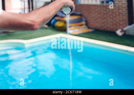 Persona che pulisce e clorurando la piscina in un caldo pomeriggio estivo, sta facendo funzionare il pulitore e aggiungendo polvere di cloro Foto Stock