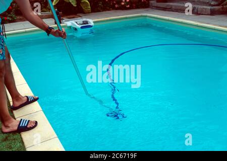 Persona che pulisce e clorurando la piscina in un caldo pomeriggio estivo, sta facendo funzionare il pulitore e aggiungendo polvere di cloro Foto Stock