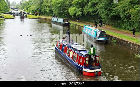 Quattro Narrow Boats che lavorano tra le serrature 76 e 75 sulle serrature Wigan, due che salono il volo e due giù, mentre una larga fascio è in lontananza. Foto Stock