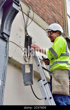 Tecnico telefonico su scala con generatore di toni che testa un nido di fili di rame per tracciare un collegamento nella scatola di derivazione dell'abitazione Foto Stock