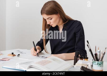 Ritratto di giovane bella signora seduta alla scrivania bianca con libro aperto mentre si scrivono note su carta isolato Foto Stock