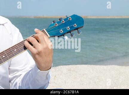 L'uomo sta suonando la chitarra sulla spiaggia di mare. Mano maschile con strumento musicale primo piano Foto Stock
