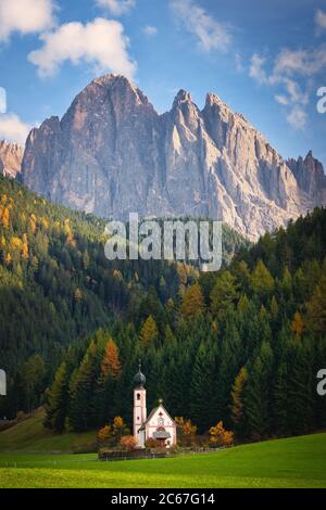 La chiesa di San Giovanni in Ranui con alle sue spalle una foresta con larici in colori autunnali e una vetta dolomitica a Sankt Magdalena, Italia. Foto Stock