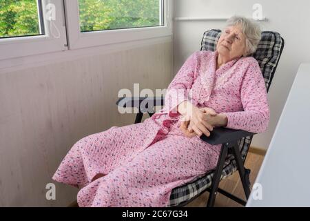 La vecchia donna anziana riposa sulla sedia sul balcone. Signora anziana seduta su una sedia morbida in terrazza. Vecchia donna che si rilassa in balcone durante la quarantena Foto Stock