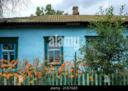 Vecchia casa in ordine blu con finestre in legno e tetto in tegole in villaggio o campagna. Dietro recinzione di legno. Il concetto di una vita quotidiana tranquilla. Selettivo Foto Stock