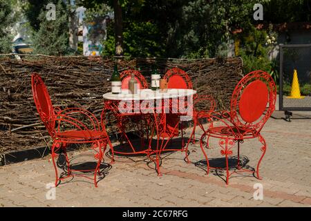 Vecchi mobili in ferro battuto rosso antico, esterno shabby chic. Set di tavolo rotondo con bottiglia di vino e tazze e sedie in giardino. Tavolo sul caffè bac Foto Stock