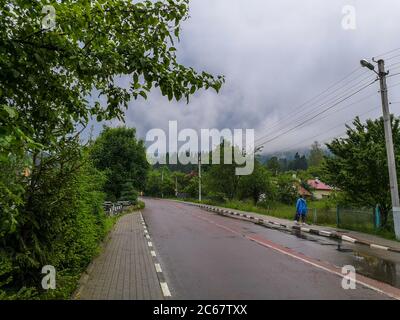 Donna pedonale in arcobaleno camminando lungo la strada di campagna in carpazi montagne. Tempo nuvoloso con nubi buie. Foto Stock