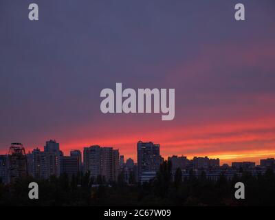 Incredibile tramonto viola, viola, rosso e giallo sulla città di Kiev (Kiev) con edifici, ruota panoramica e chiesa a cupola all'orizzonte. Paesaggio urbano industriale Foto Stock