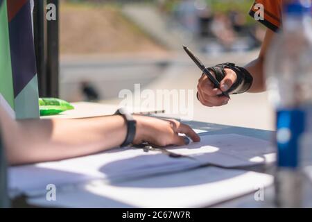 Primo piano di giovani adolescenti che si iscrivano a una gara di skateboard all'aperto. Mano con stecca da polso modulo di registrazione per sport estremi co Foto Stock