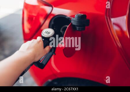 Donna che pompa benzina in auto alla stazione di rifornimento. Il cliente della stazione di servizio detiene l'automobile che rifornisce l'ugello. Foto Stock