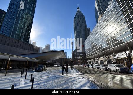 Davanti alla strada fuori dalla Meridian Hall, guardando verso la CN Tower in un giorno limpido degli inverni. Due persone che camminano nella neve avvolta in abiti invernali. Foto Stock