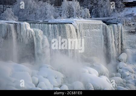 Cascate americane e cascate Bridal Veil durante l'inverno. Alberi congelati e massi e neve sul terreno. Nebbia che si alza dalle cascate. Cascate del Niagara. Foto Stock