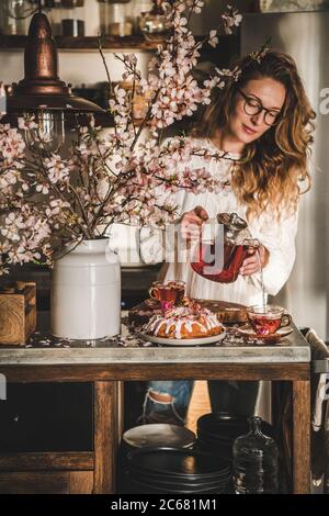 Donna che versa il tè in tazze sopra il tavolo con la torta di ciambella Foto Stock