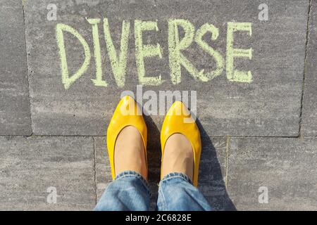 Concetto diversificato, vista dall'alto sulle gambe della donna e testo scritto in gesso sul marciapiede grigio Foto Stock