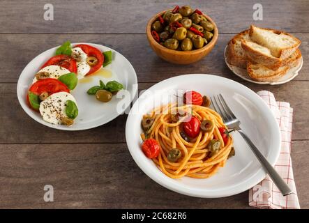 Tavolo completo di piatti italiani su piatti. Spaghetti, caprese, olive e pane. Foto Stock