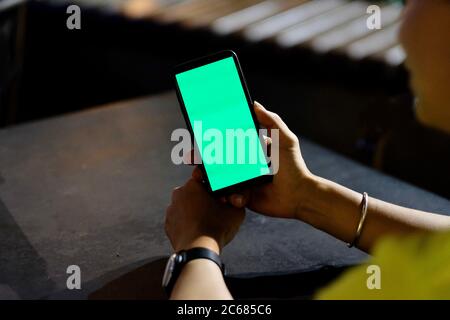 Vista a spalla di un giovane uomo che guarda lo smartphone a schermo verde all'aperto di notte. Sfocatura dello sfondo Foto Stock