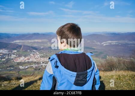 ragazzo sulla schiena guarda il paesaggio in autunno con un cappotto blu Foto Stock