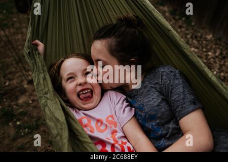 Sorella grande che baciava la sorellina in amaca all'esterno Foto Stock