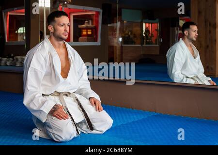 Uomo Karate con tradizionale postura giapponese seduta su tatami. Indossa il kimono bianco Foto Stock