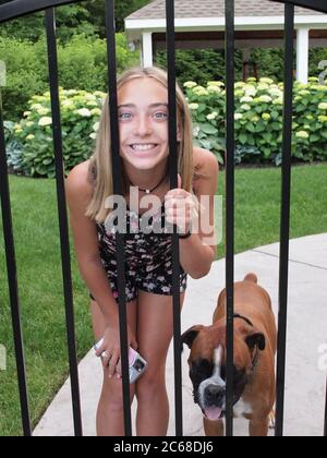 Ragazza di dodici anni che sbirciando attraverso recinzione con il suo Boxer animale domestico. Foto Stock