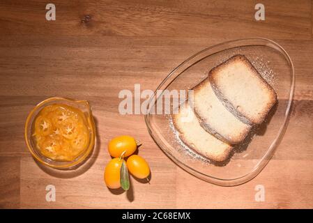 Kumquat canditi e freschi, e fette di torta di agrumi su lastre di vetro, su una superficie di legno. Vista dall'alto Foto Stock