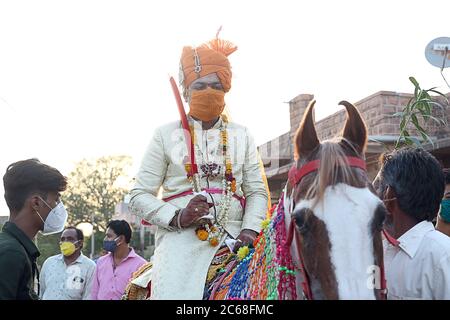 Jodhpur, Rajashtbn, India. 30 giugno 2020: Sposo indiano indossare maschera protettiva con spada in mano seduta a cavallo, baarat lock down finisce con m di sicurezza Foto Stock