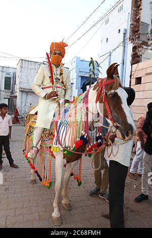 Jodhpur, Rajashtbn, India. 30 giugno 2020: Sposo indiano indossare maschera protettiva con spada in mano seduta a cavallo, baarat lock down finisce con m di sicurezza Foto Stock