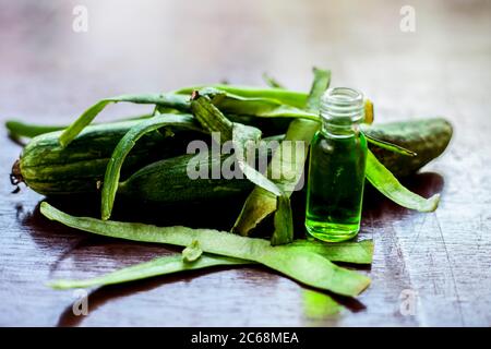 Primo piano di olio essenziale fresco o di zucca di spugna o di luffa in una bottiglia di vetro insieme con una zucca di spugna fresca sulla superficie marrone. Foto Stock