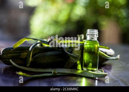 Primo piano di olio essenziale fresco o di zucca di spugna o di luffa in una bottiglia di vetro insieme con una zucca di spugna fresca sulla superficie marrone. Foto Stock