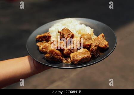 Salate ossa di maiale stufate con riso servite su piatto nero Foto Stock