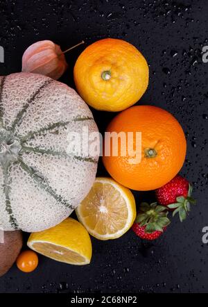 Melone di melone, arance, limoni, fragole e lanterna cinese su sfondo nero. Foto Stock