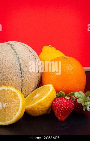 Melone di melone, arance, limoni e fragole davanti a una parete rossa. Foto Stock