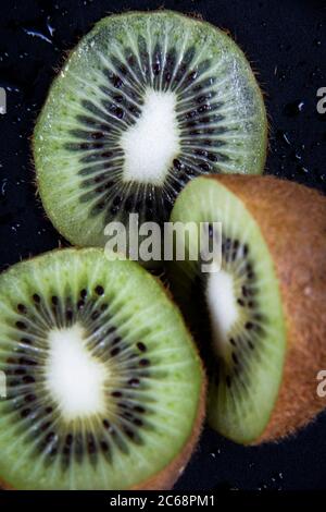 Un'immagine ravvicinata di alcune fette di kiwi fresche su sfondo nero umido. Foto Stock