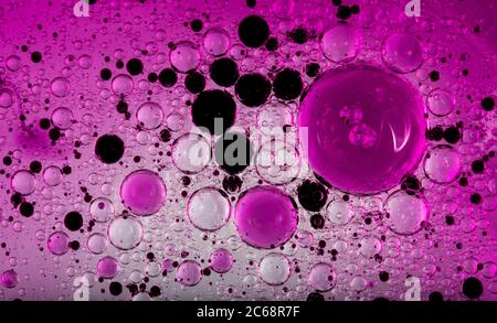 Bolle d'olio nell'acqua. Colori rosa e viola e nero. Foto Stock