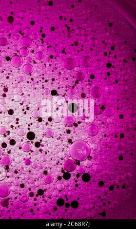 Bolle d'olio nell'acqua. Colori rosa e viola e nero. Foto Stock