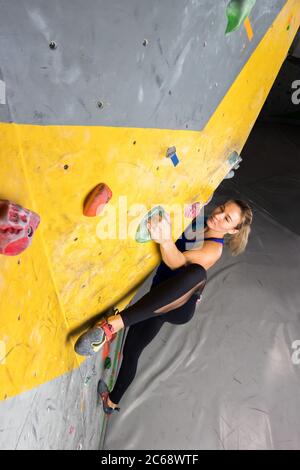 Donna scalatore di roccia appesa su una parete di arrampicata bouldering, all'interno su ganci colorati. Foto Stock