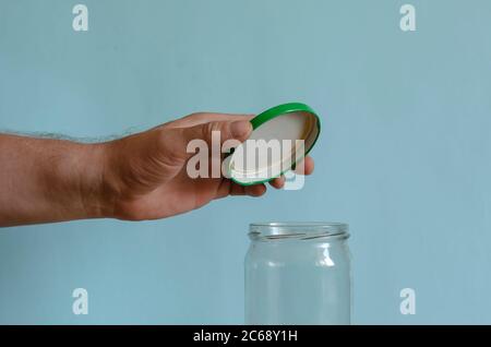 La mano chiude un vaso di vetro vuoto con un coperchio verde metallico. Mano dell'uomo su un vaso di vetro. Uomo di razza europea di mezza età. Confezionamento alimentare Foto Stock