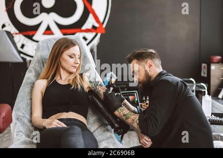 Tatuatore professionale che fa tatuaggio sulla mano della ragazza usando la macchina del tatuaggio in studio moderno Foto Stock