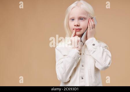 bambino sognante pensoso con sindrome albinismo che parla al telefono con un amico, ascoltando notizie al telefono, stare in piedi guardando il lato. isolato Foto Stock