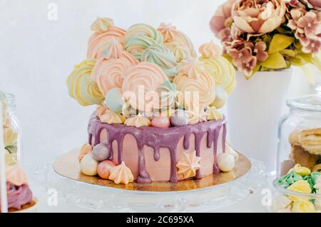 Bella torta festiva con meringhe colorate e smalto violetto. Rosa, giallo, viola, verde. Foto Stock