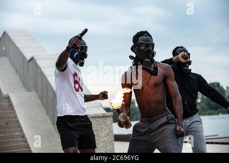 tre persone con pelle scura in maschera si oppongono all'antirazzismo, tengono in mano una bottiglia di fuoco, gridano per le strade Foto Stock