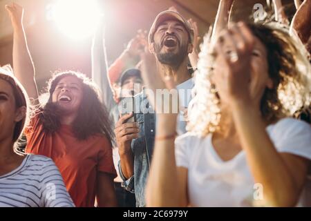Un grande gruppo di tifosi di calcio che urla e che si acclamano per la loro squadra. Eccitati gli appassionati di sport in piedi con le mani sollevate e. Foto Stock