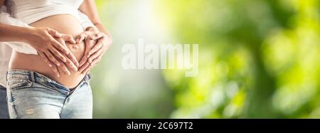 Donna incinta con suo marito che la abbrancava. Mani di futuri genitori in previsione del bambino che abbrancano una pancia a forma di cuore Foto Stock