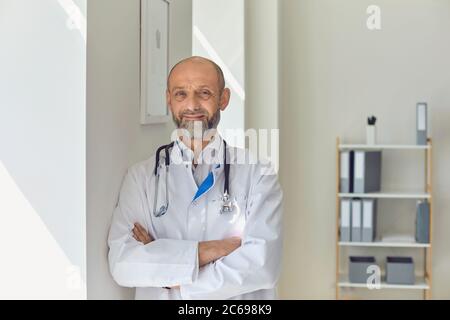 Medico anziano con braccia incrociate in un moderno ufficio clinico. Foto Stock