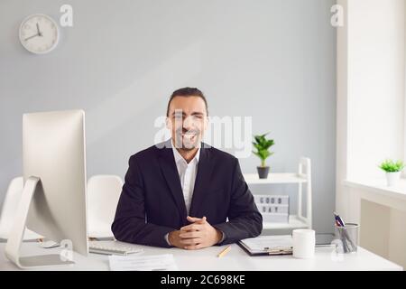 Un uomo brunette in una giacca nera seduta al tavolo lavora con le carte in ufficio. Foto Stock