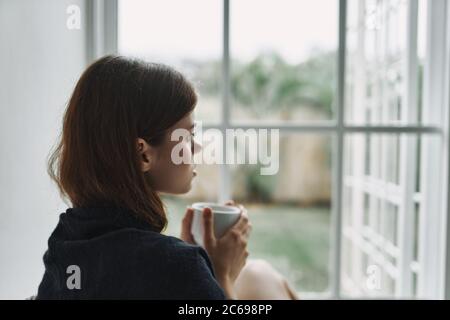 Una donna con una plaid sulle spalle si trova vicino alla finestra Foto Stock