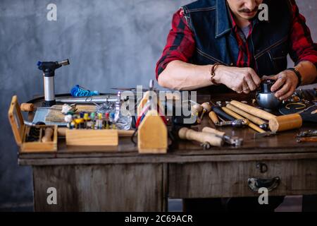 primo piano su foto ritagliata. giovane uomo che attacca il gioiello nel metallo d'oro, copia spazio. ragazzo specializzato nel lavoro con il metallo Foto Stock